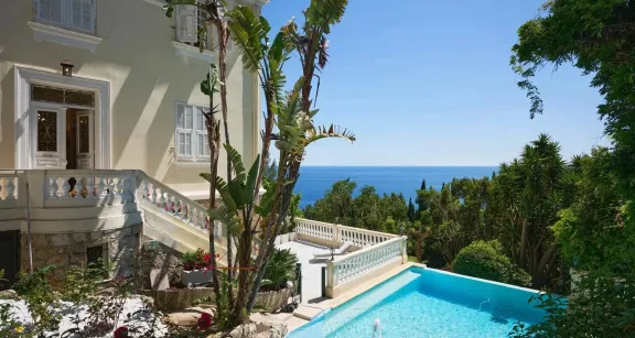 Elegant villa with lush gardens, turquoise pool, and panoramic sea view near Monaco, featuring classic architecture and detailed stonework.