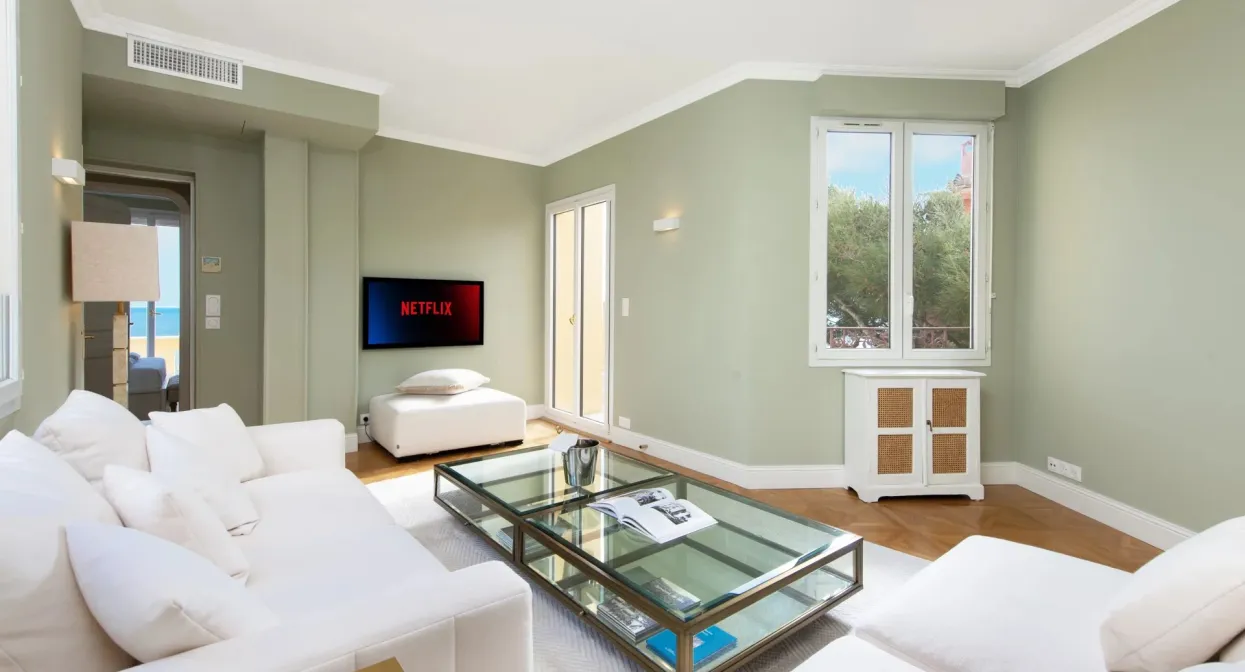 Просторная гостиная пентхауса с мягкой белой мебелью, стеклянным журнальным столиком и видами на море через большие окна, создающее ощущение лёгкости и уюта.