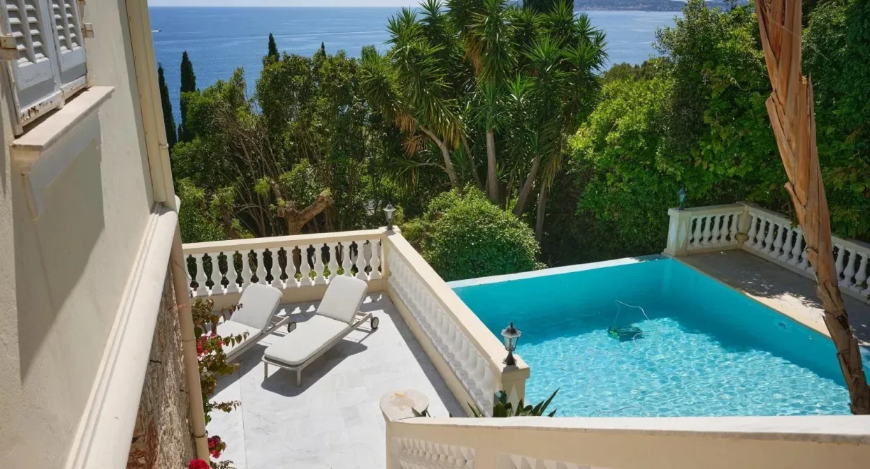 Elegant villa terrace with lush greenery, pristine pool, and stunning Mediterranean Sea views; perfect for luxurious relaxation.