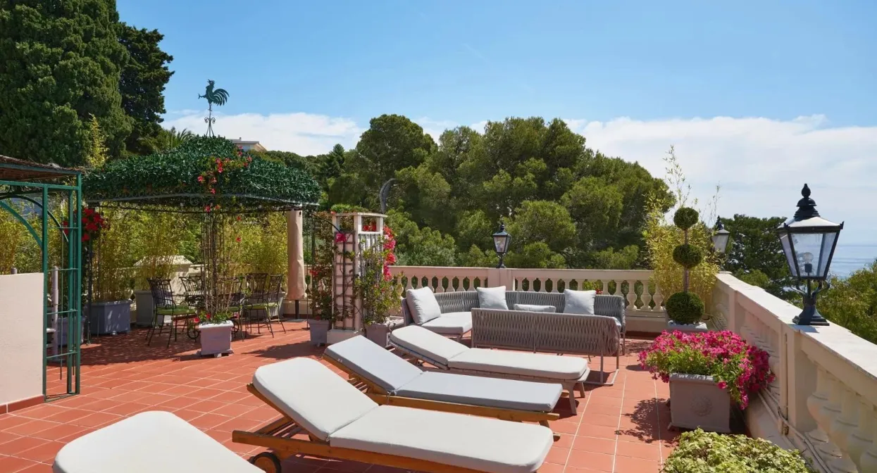 Spacious terrace with sun loungers, lush greenery, trellised pergola, and ocean views; elegant ambiance near Monaco.