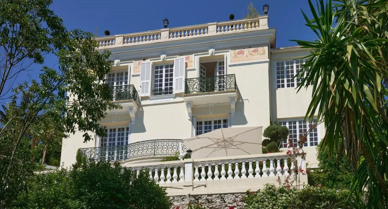 Elegant villa with ornate iron balconies, lush garden, and classic architecture, enjoying sunlit terraces and proximity to Monaco.