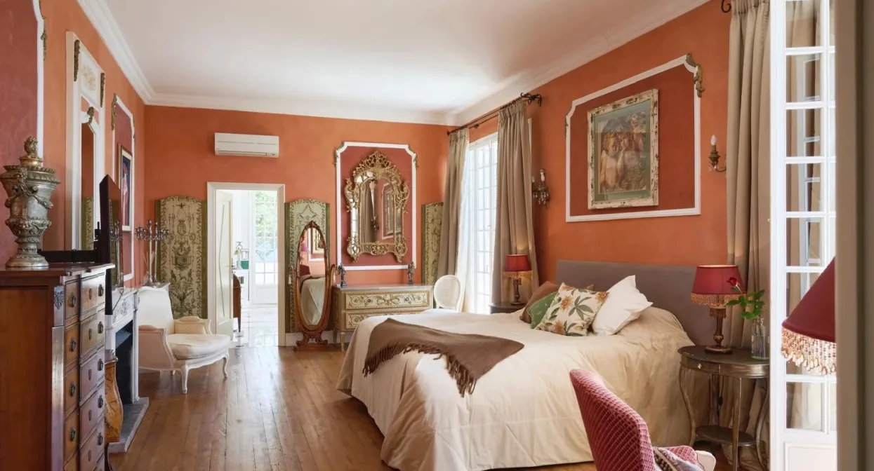Spacious villa bedroom with warm earthy tones, vintage decor, elegant furnishings, large windows, and a view of the lush garden.