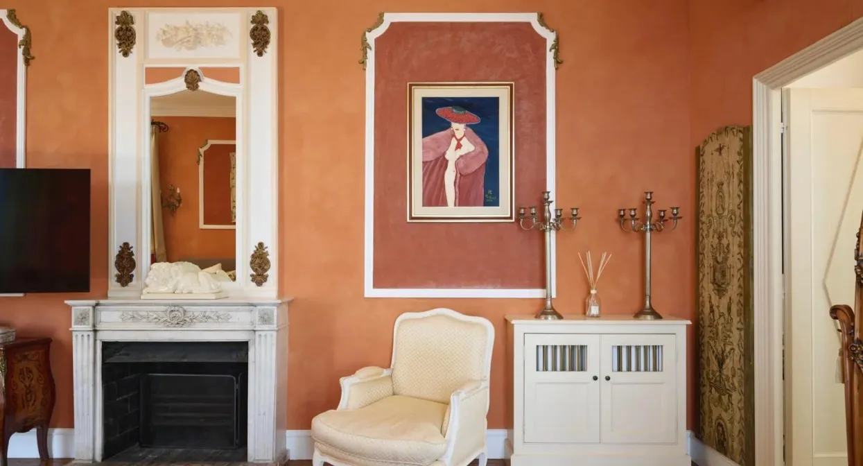 Elegant living room with terracotta walls, ornate fireplace, classic armchair, and sophisticated decor, creating a warm, luxurious ambiance.