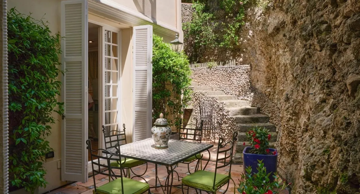 Charming courtyard with wrought iron furniture, lush greenery, and rustic stone walls creates a serene outdoor dining space near Monaco's border.